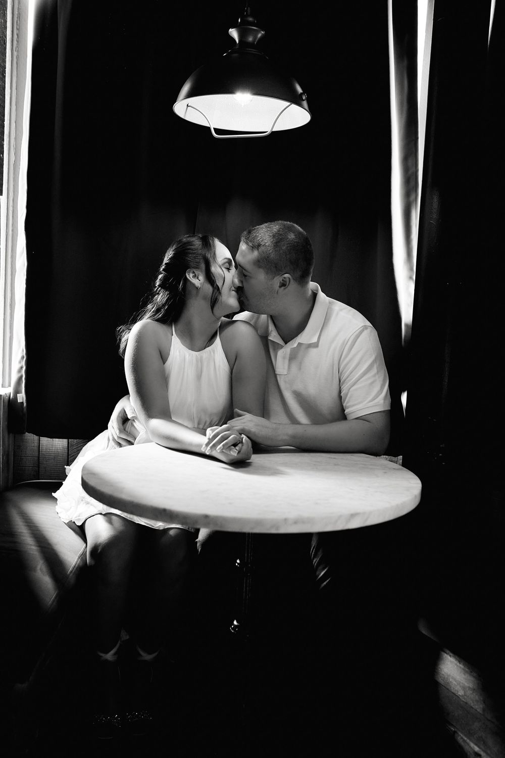 A romantic couple shares an intimate moment at a small round table under moody lighting.