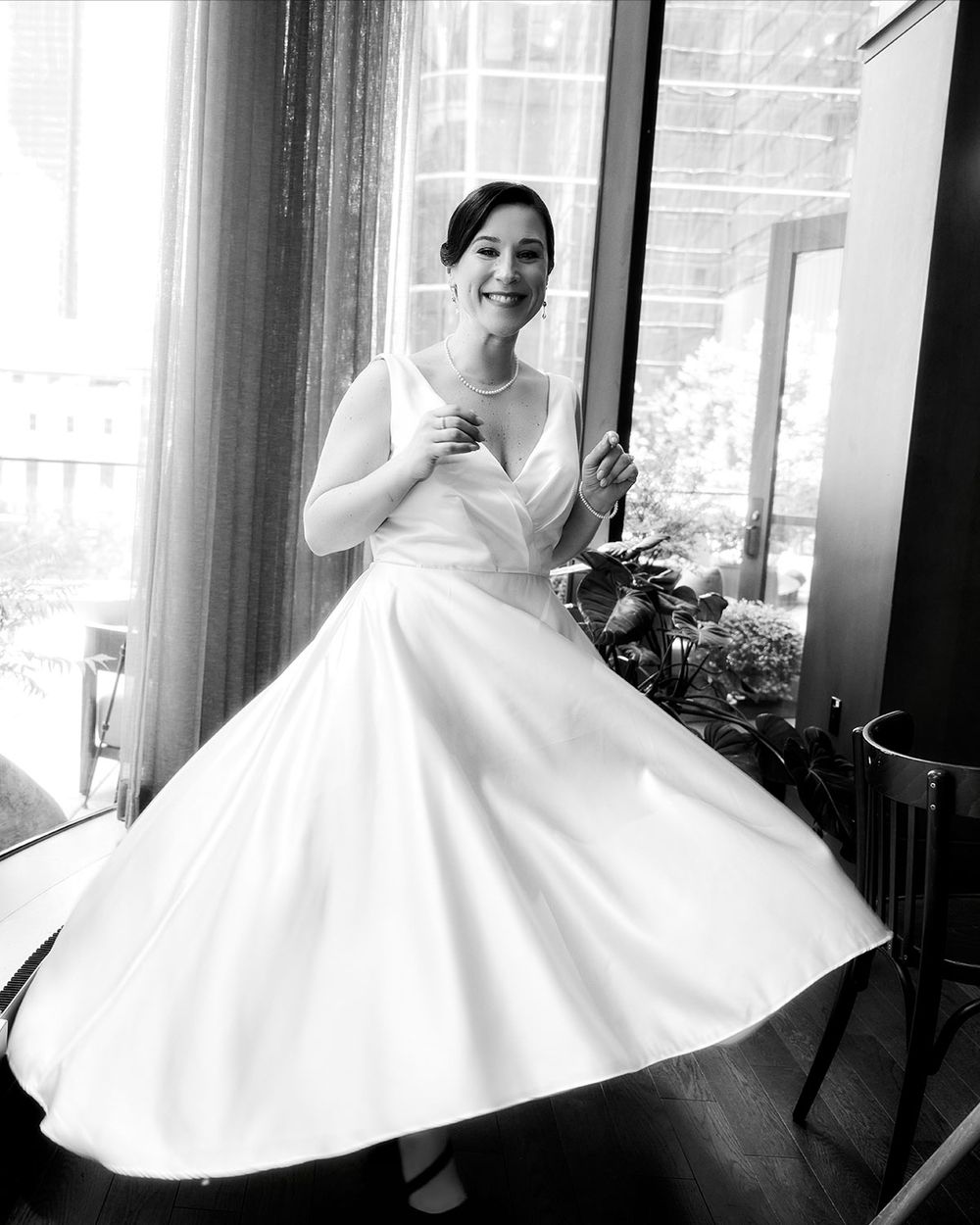 Bride in a classic white ball gown twirls gracefully in front of large windows.