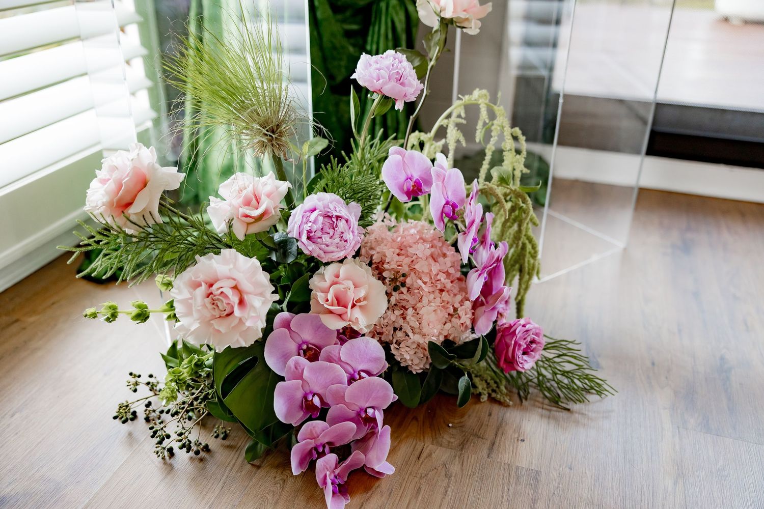 Pink and white floral arrangements with evergreen sprigs are displayed in glass vases on a marble countertop.
