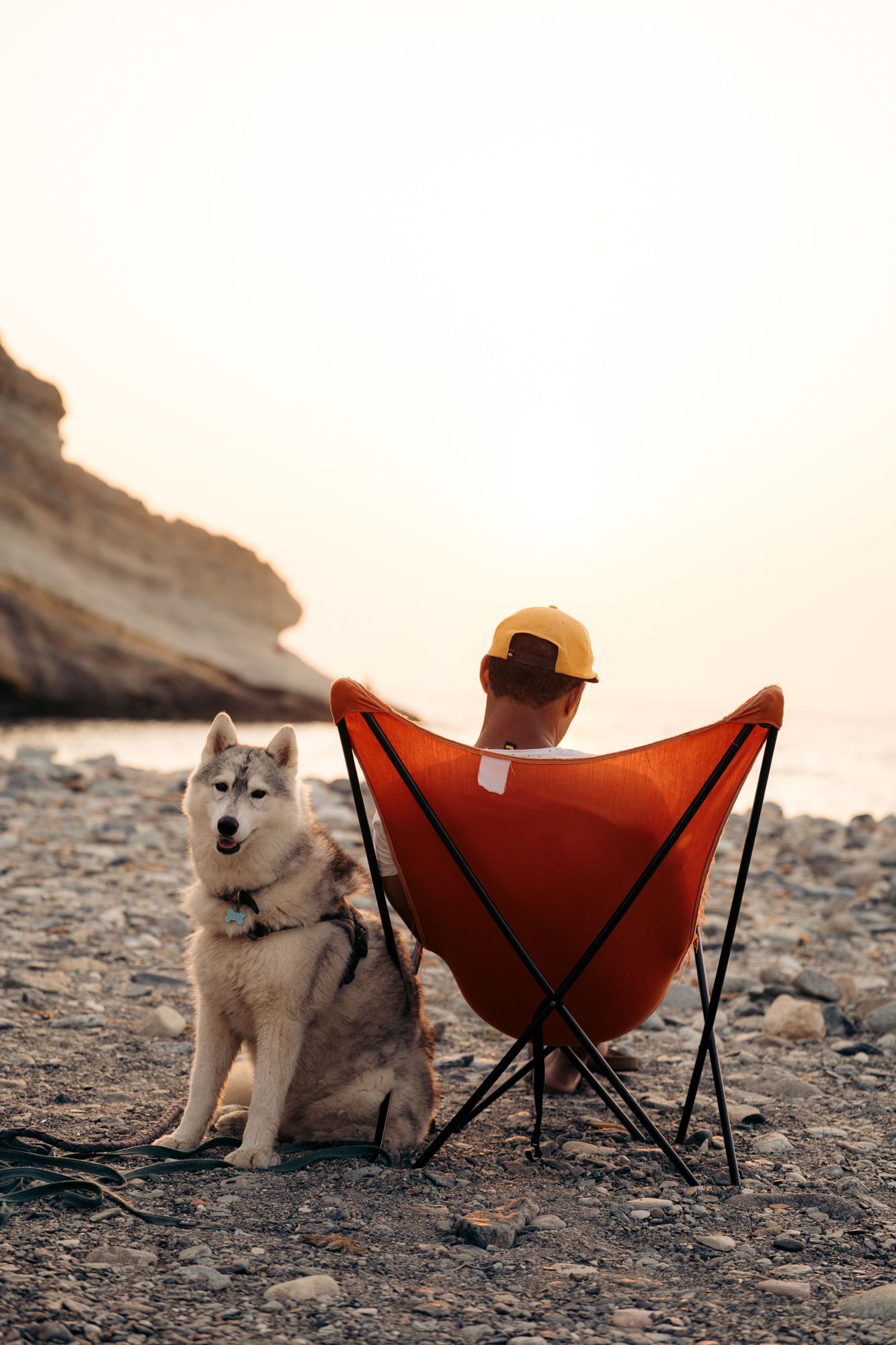 homme dans son transat avec son husky au coucher du soleil sur une plage du cap corse