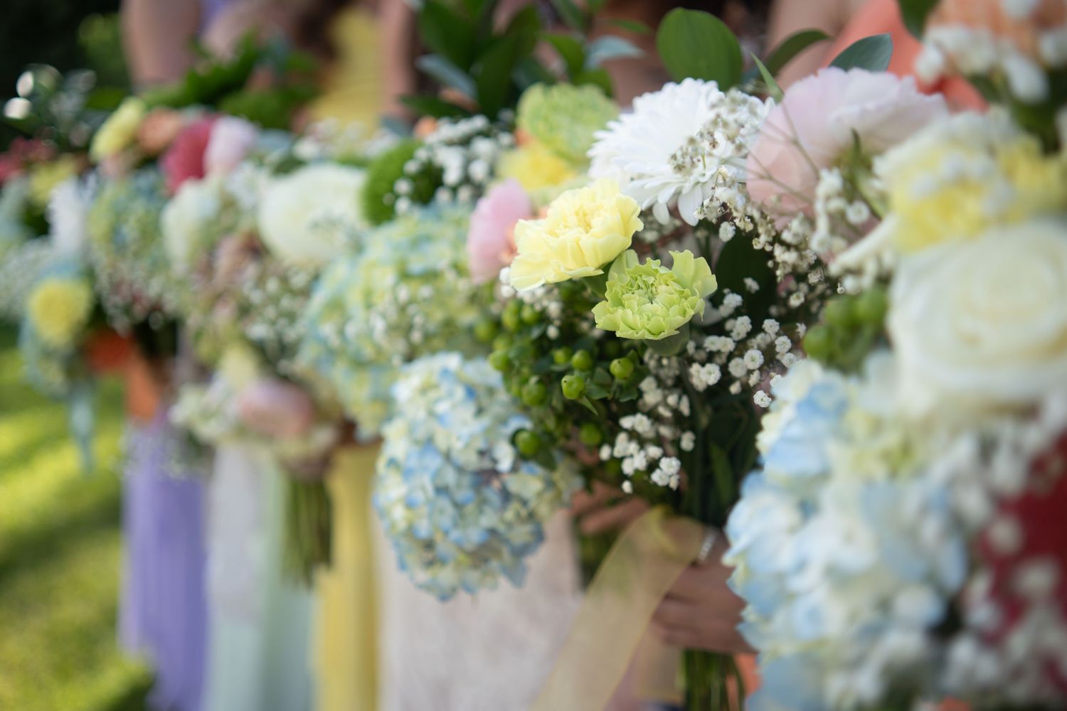 A row of elegant wedding bouquets with soft pastel flowers including hydrangeas, roses and baby's breath in natural light.