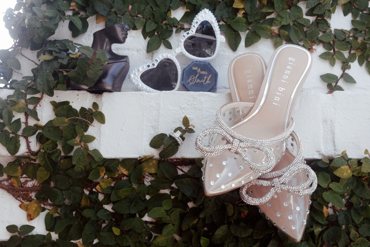 Wedding decorations featuring heart-shaped sunglasses, delicate accessories, and ivy leaves arranged on a light surface.