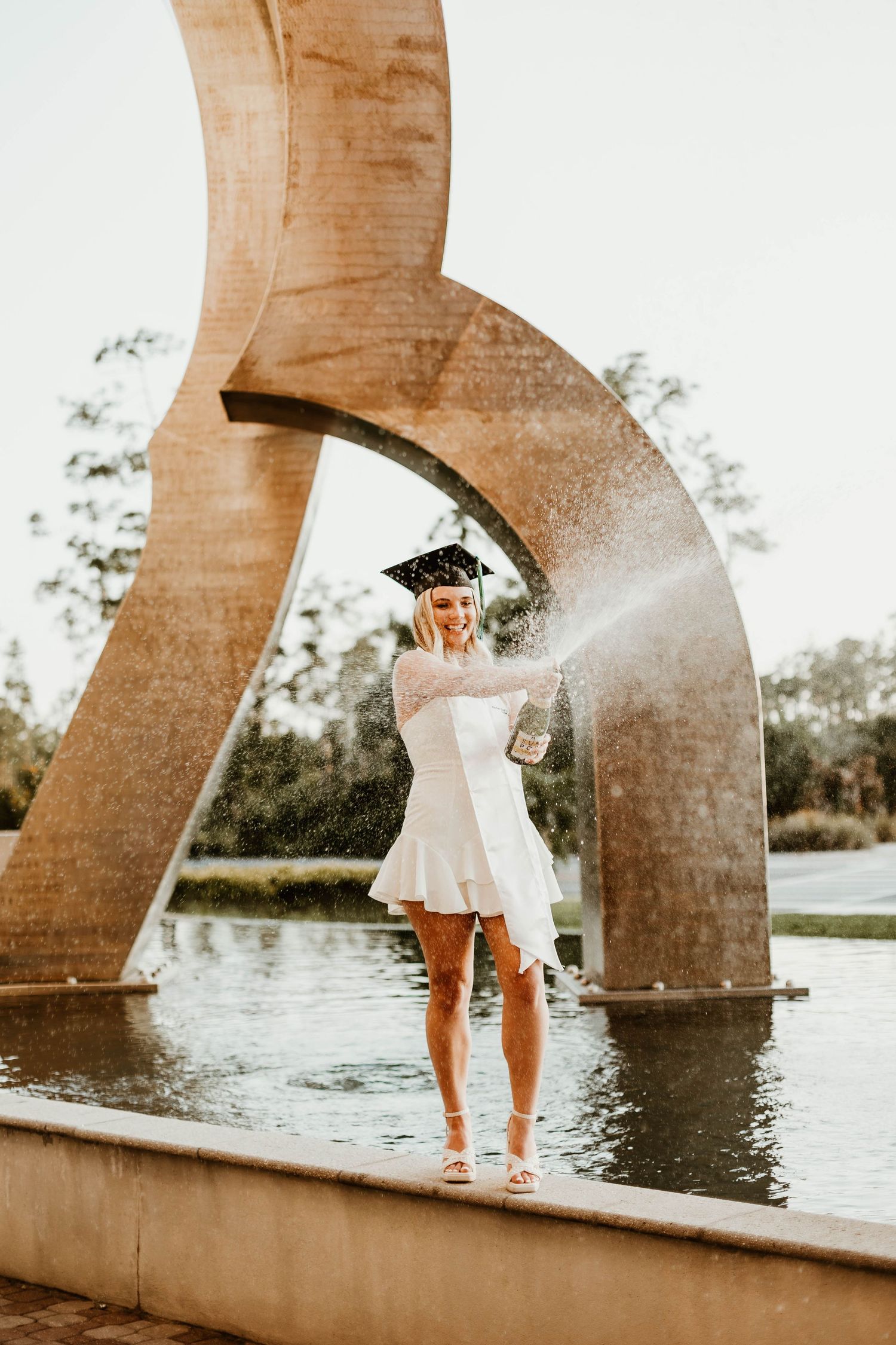 Person in a white dress standing near a bridge over water during golden hour.