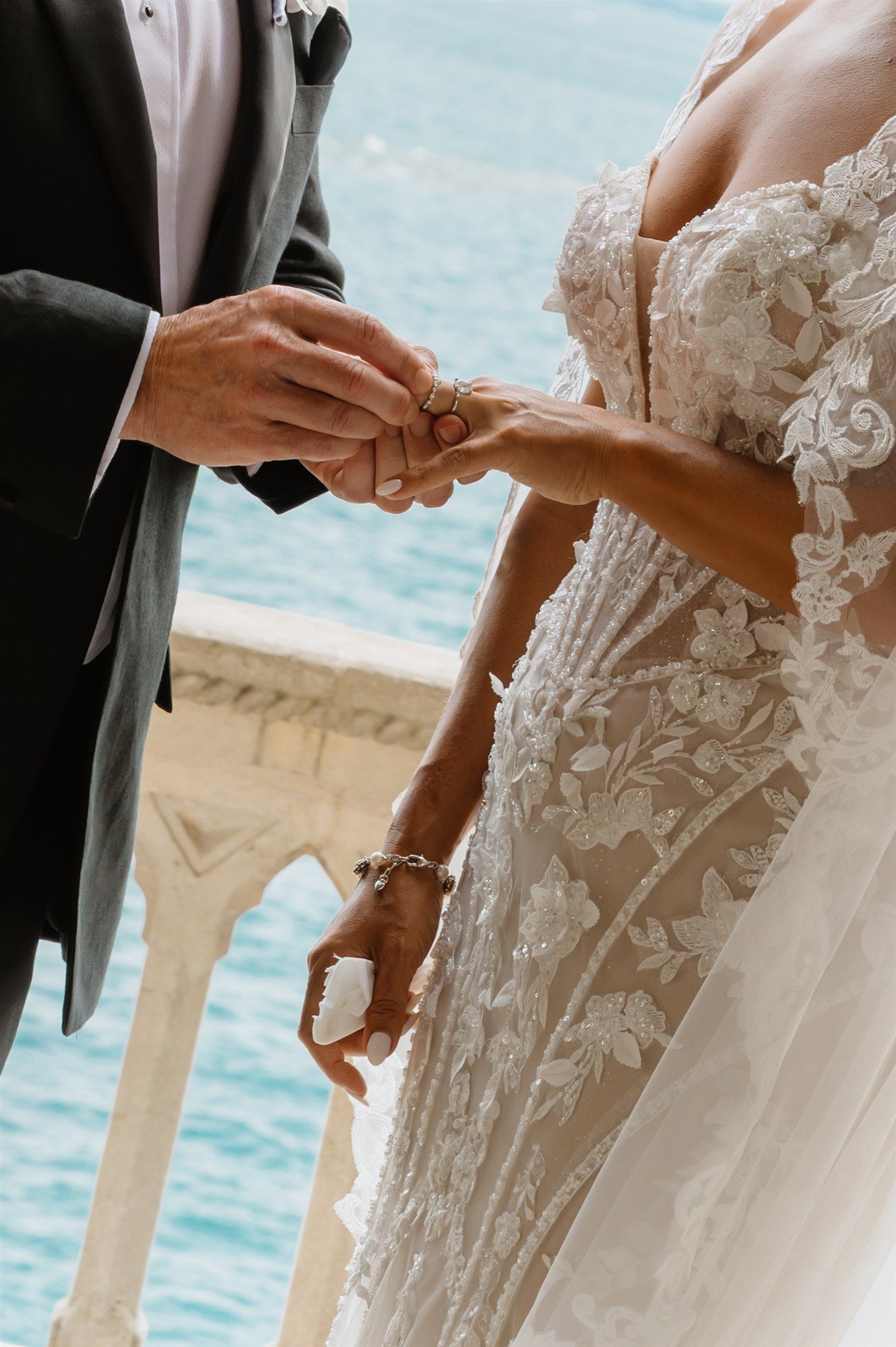 Close-up of intricate lace wedding dress details against ocean backdrop.