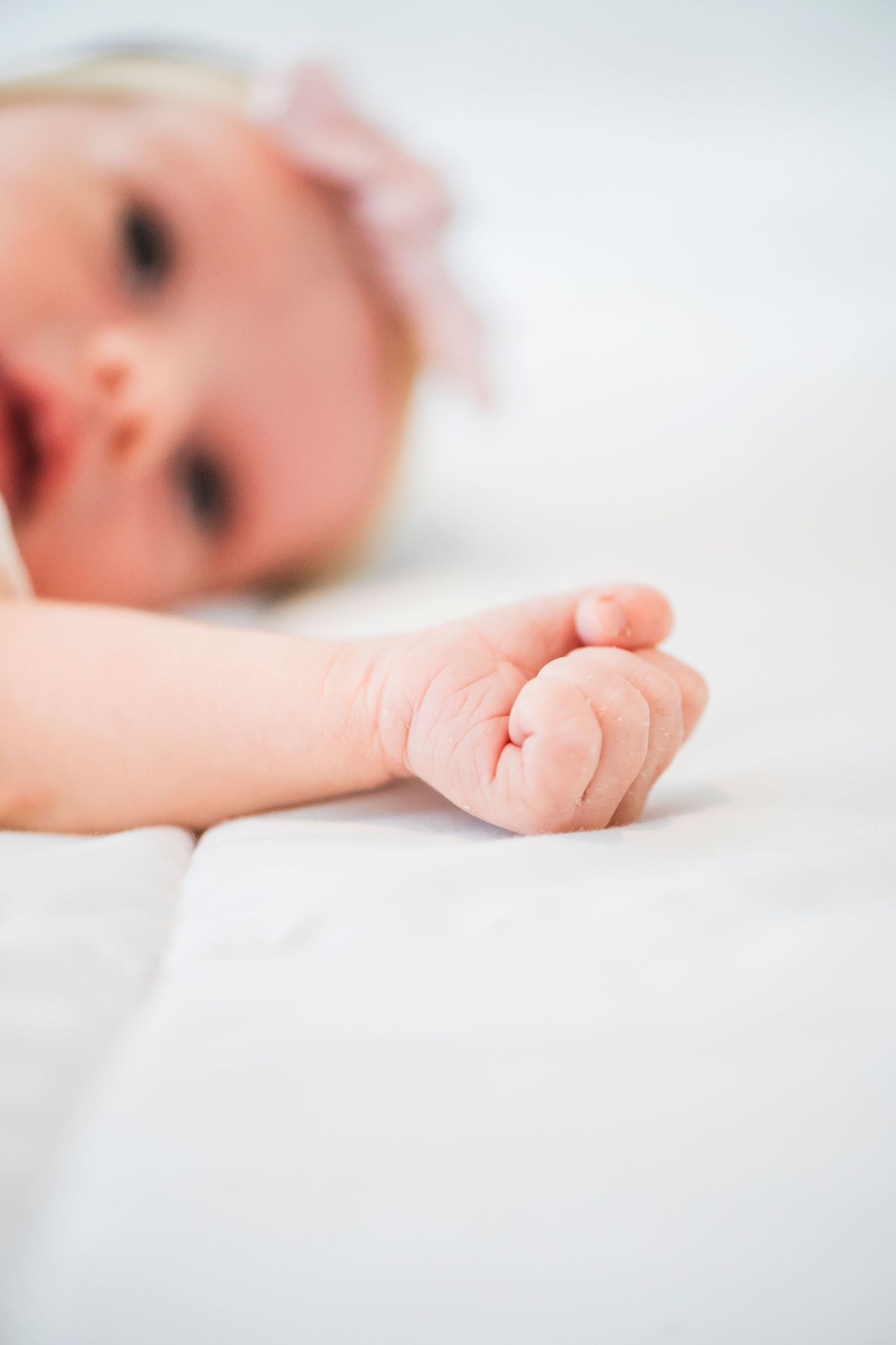 A set of four closeup artistic photos of a sleeping newborn baby on white bedding, highlighting tiny hands and feet.