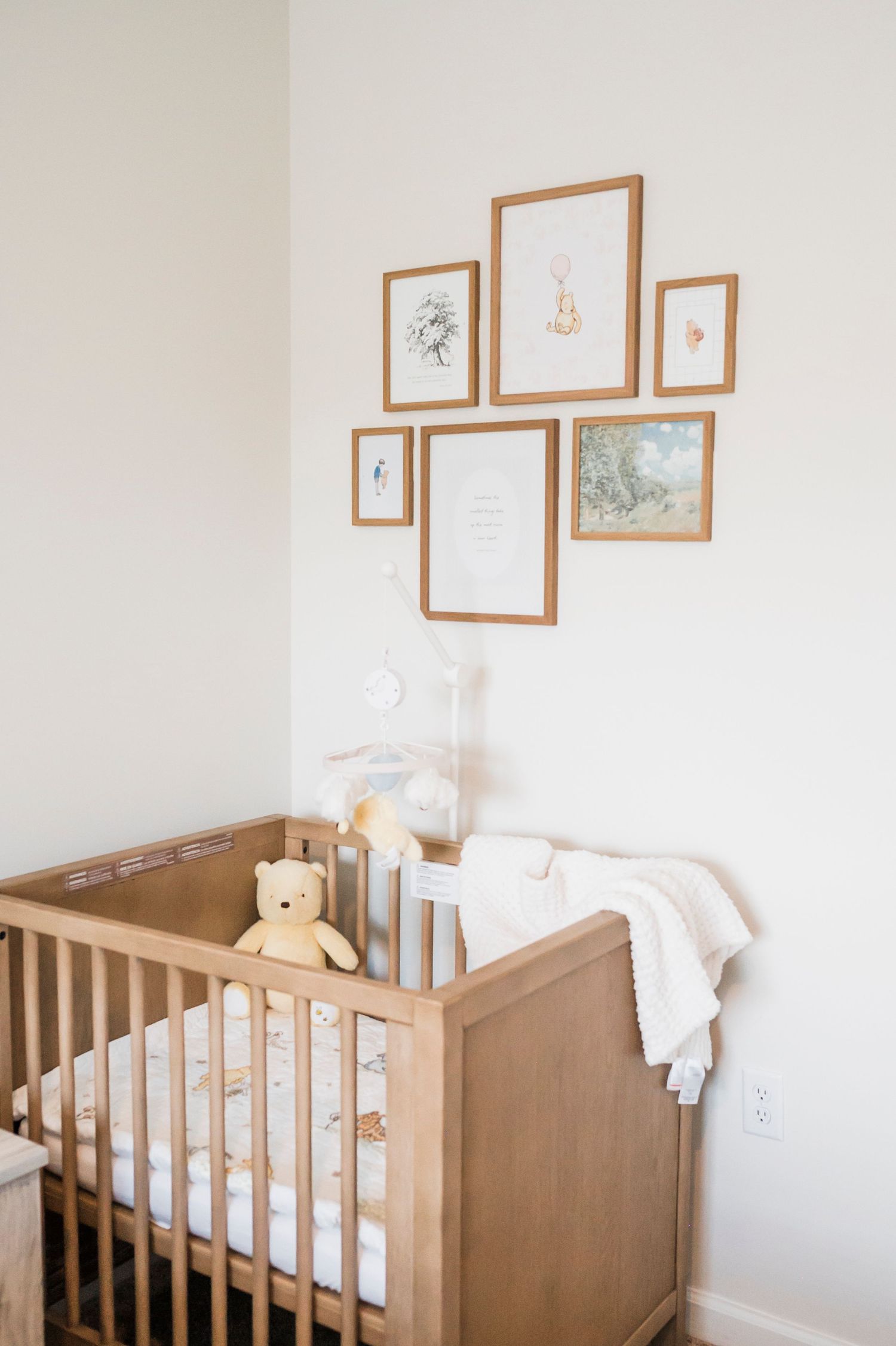 A neutral-toned nursery corner featuring a wooden crib, soft bedding, and framed wall art in delicate pastel colors.