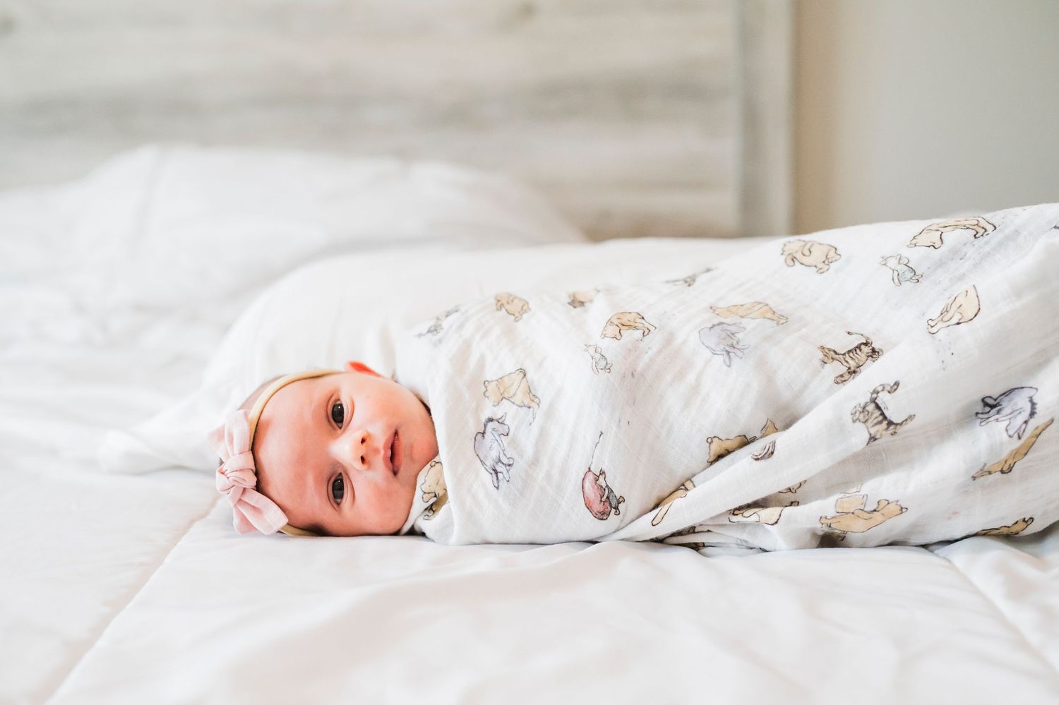 Sweet newborn baby lying on white bed wearing soft floral onesie in peaceful nursery setting.