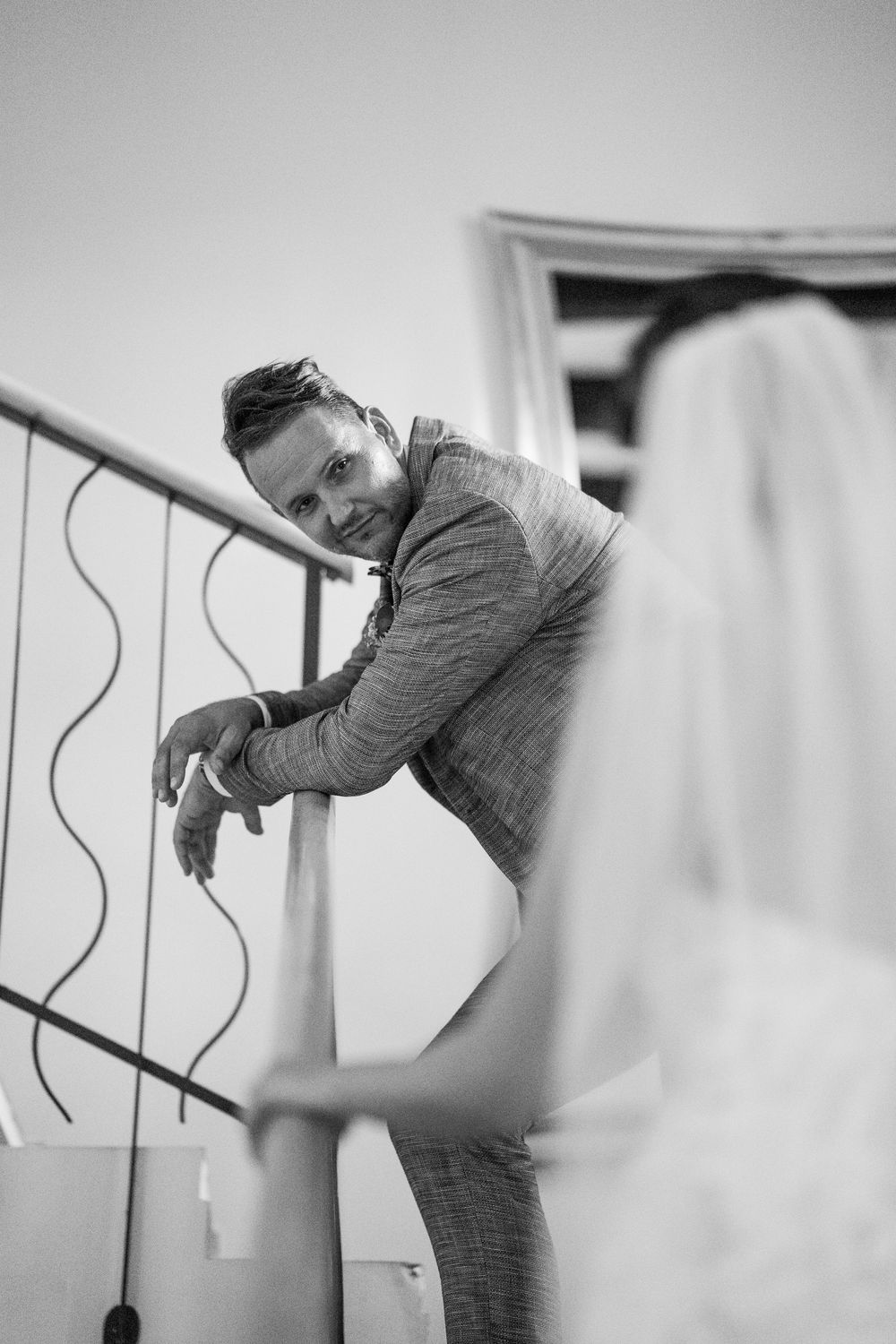 A black and white photo capturing a candid moment as someone leans over a staircase railing in casual attire.