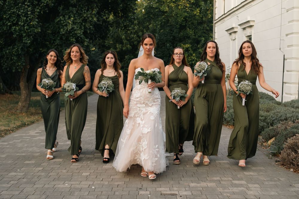 Bridal party in olive green dresses walks and laughs together during outdoor wedding photo session.
