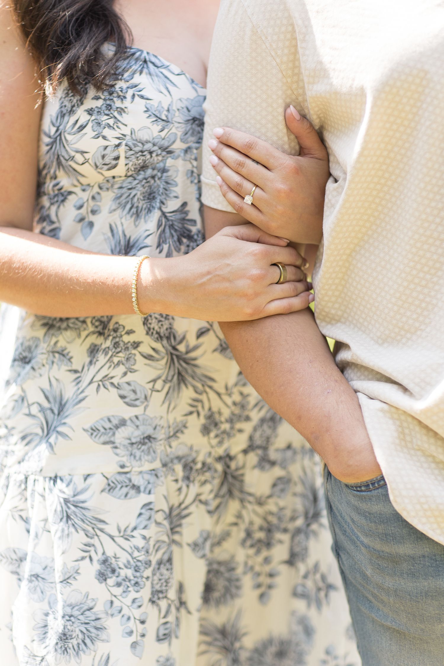 A romantic couple embracing in soft light wearing floral print dress and denim while hugging closely together.