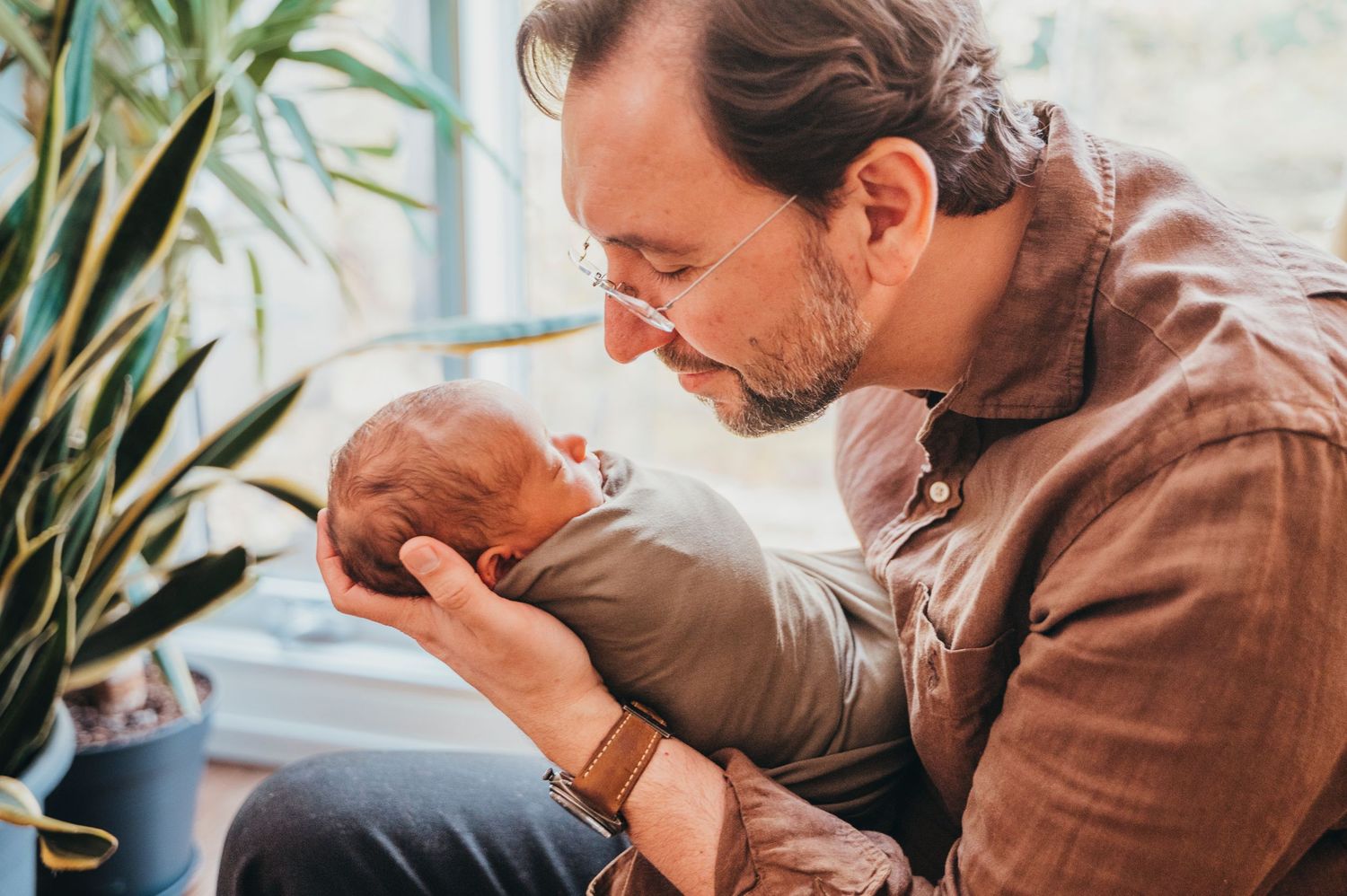 Dad cradles baby's head and holds her face close to his while smiling and looking at her in their Toronto home