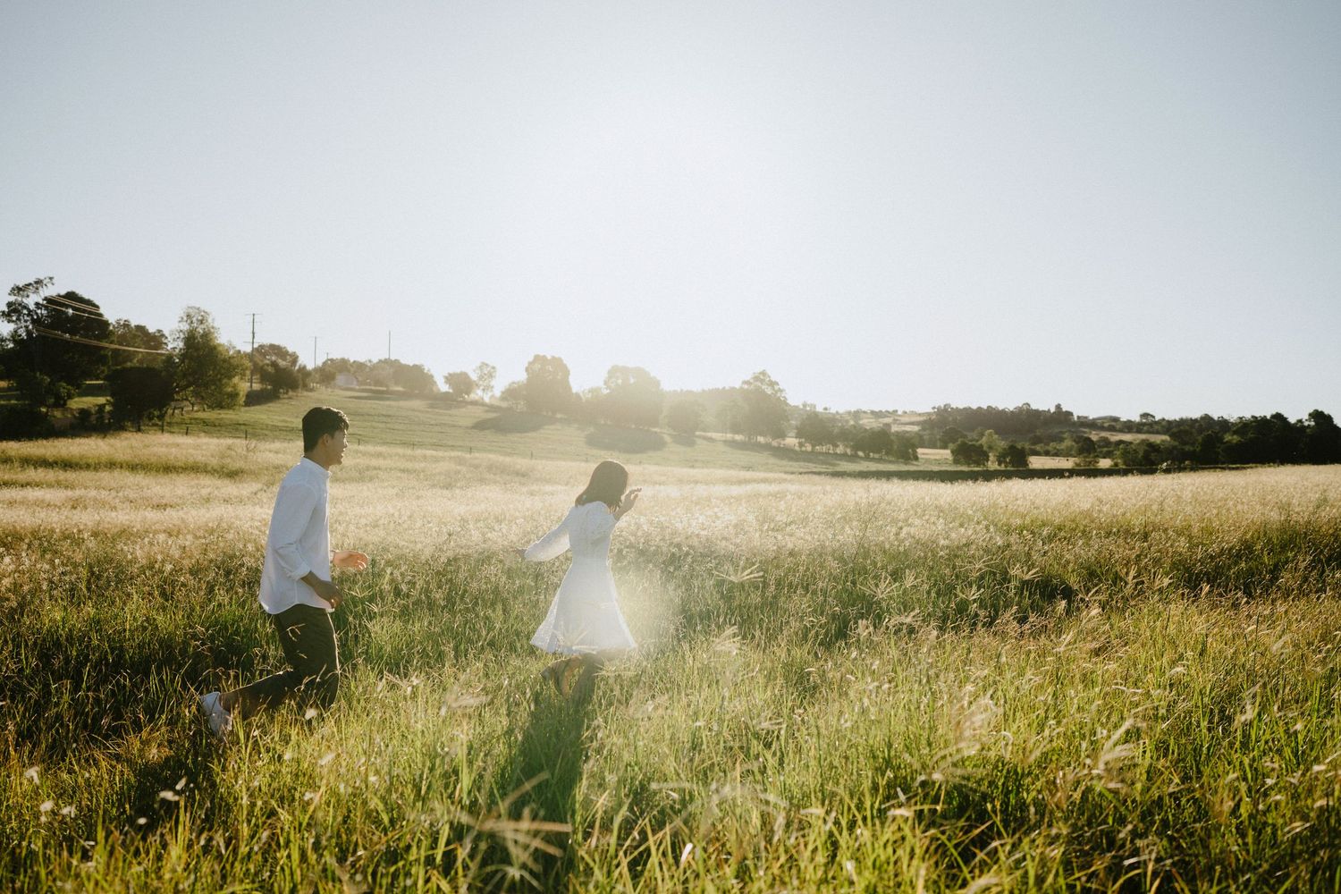 Two people joyfully leap in unison against a sunlit hillside in a dreamy black and white moment.