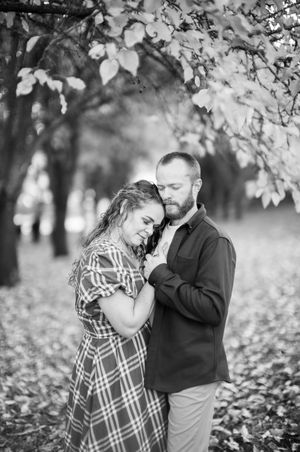 Romantic autumn portrait of a couple embracing under falling leaves in a dreamy black and white setting.