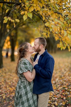 Intimate couple sharing a tender kiss beneath golden autumn foliage in a park setting.