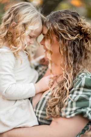 Tender moment between parent and child with curly hair touching foreheads in warm autumn light.
