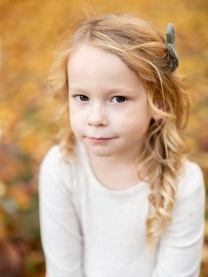 Warm autumn portrait of a child in white clothing with soft natural lighting and golden fall foliage in background.