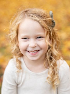 A joyful young child wearing a white sweater poses outdoors against a warm golden autumn background.