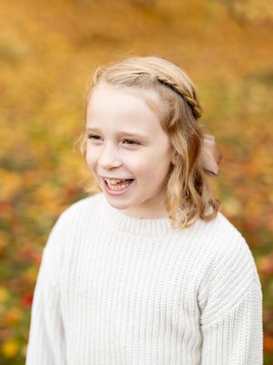 Individual wearing a white knitted sweater smiling against a warm autumn background with golden bokeh lighting.