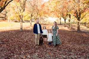 A group stands together on fallen autumn leaves in a park with golden trees in the background.