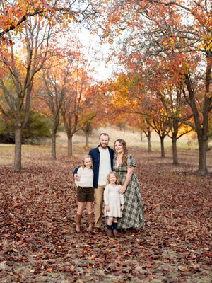 A group stands together in a beautiful autumn setting with orange and yellow trees and fallen leaves surrounding them.