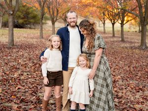 A loving family of four poses together in a fall setting with orange trees and fallen leaves covering the ground.