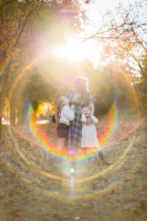 Beautiful lens flare effect creates circular rainbow rings around people walking in an autumn forest at sunset.