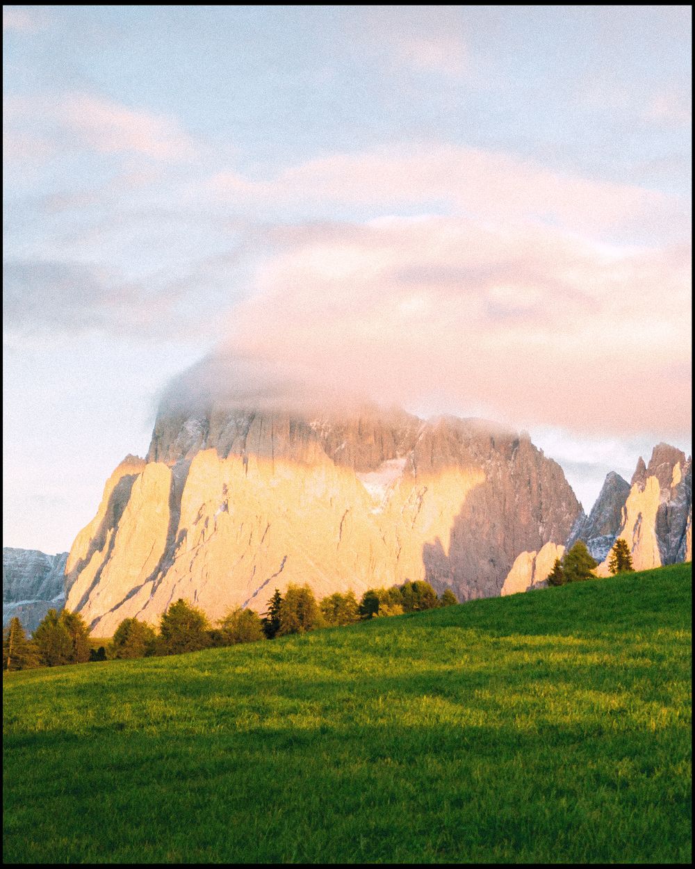 Sunlit mountain peak rising from green meadow, Dolomites
