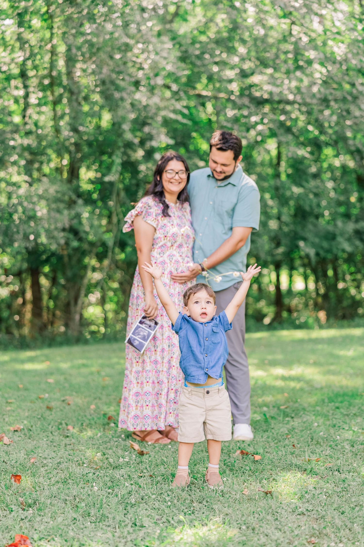 A happy family poses together on a grassy lawn with trees in the background.