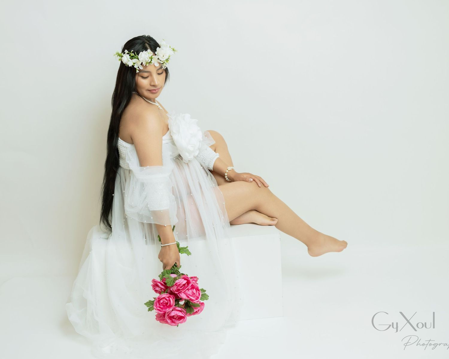 A romantic bridal boudoir photo with white sheer fabric, a floral crown and pink roses against a light background.