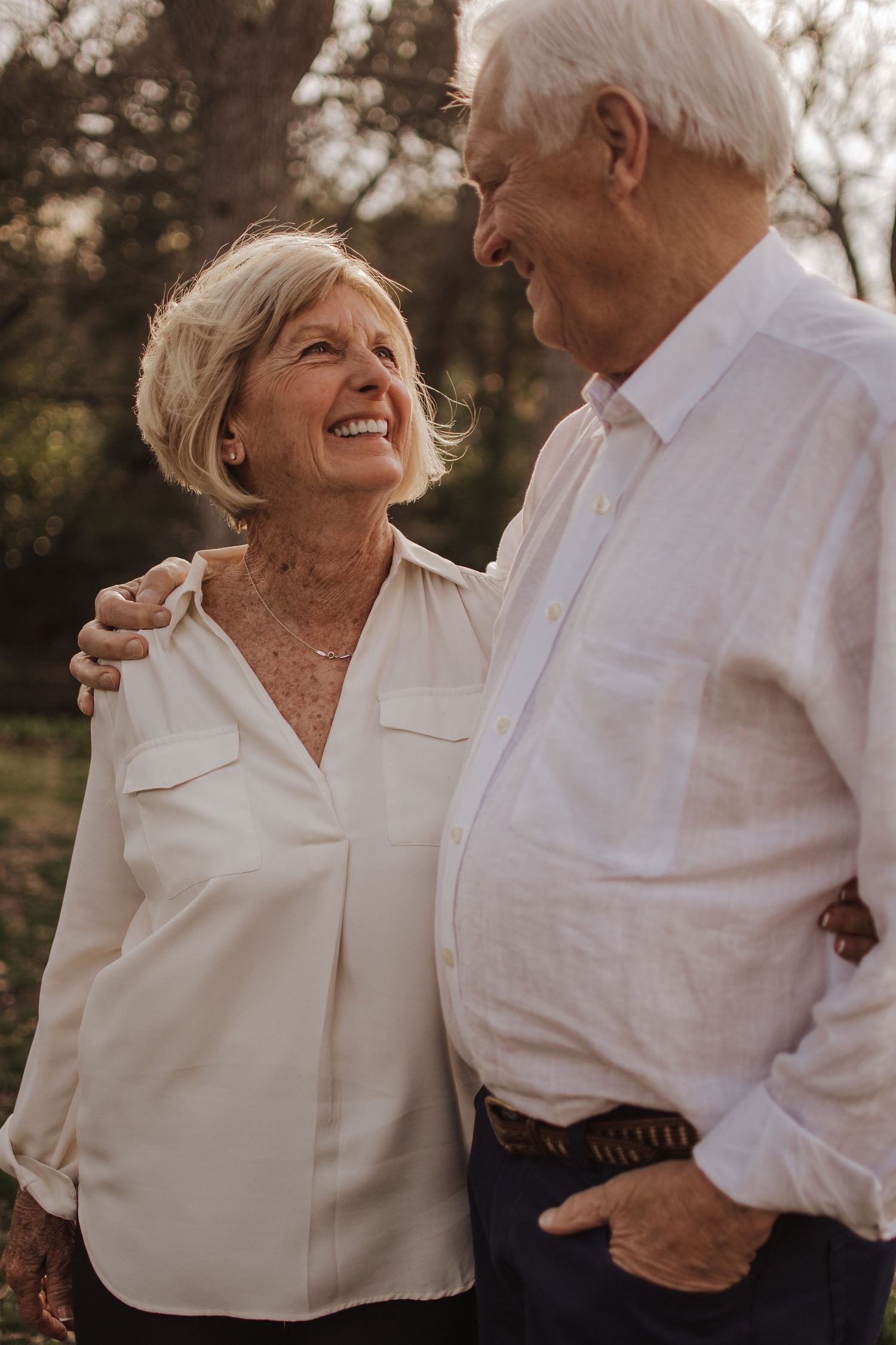 Senior couple in white shirts share loving moments outdoors during a romantic sunset photoshoot.