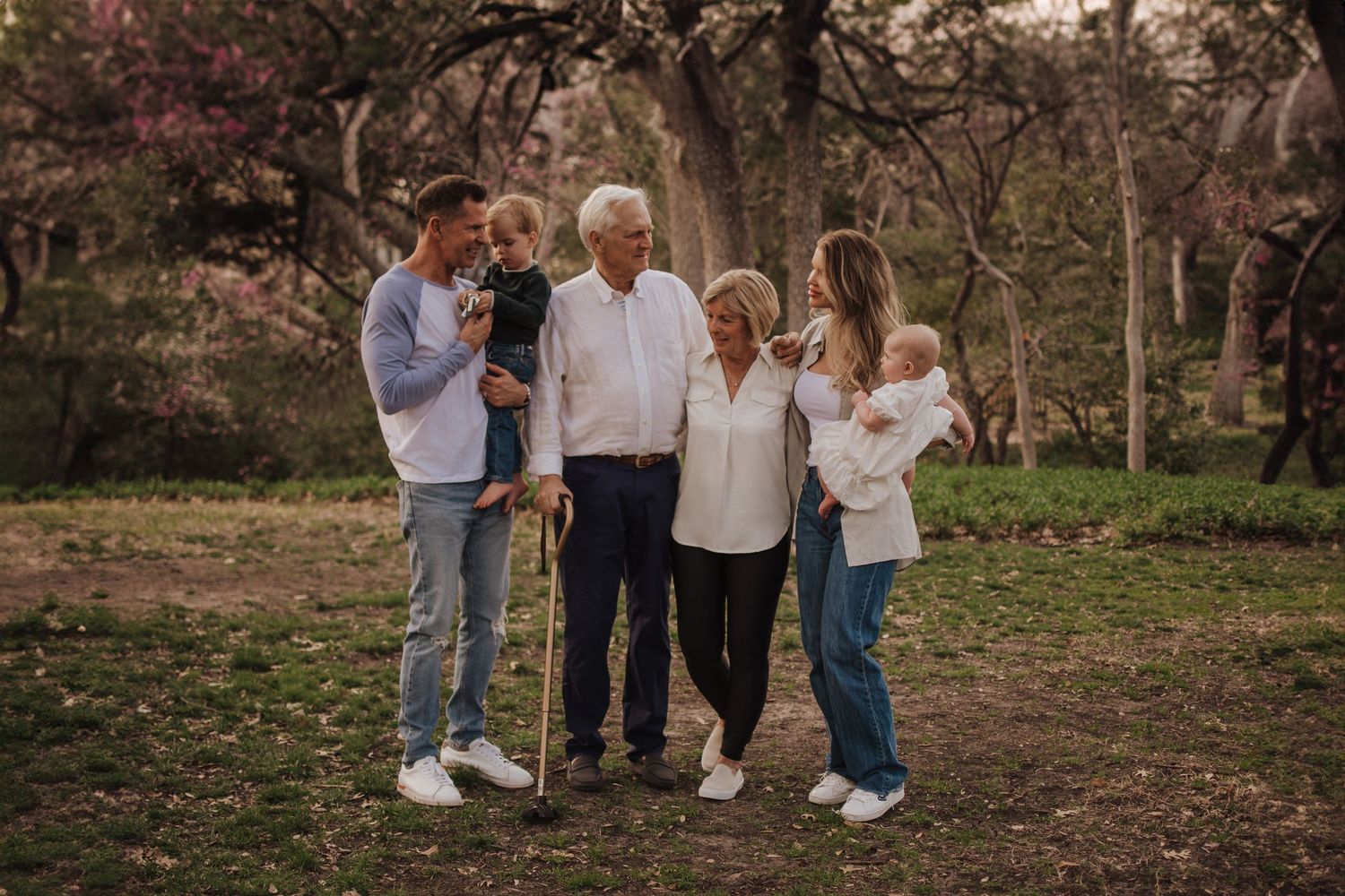 Family group standing together outdoors in an autumn garden setting during golden hour.