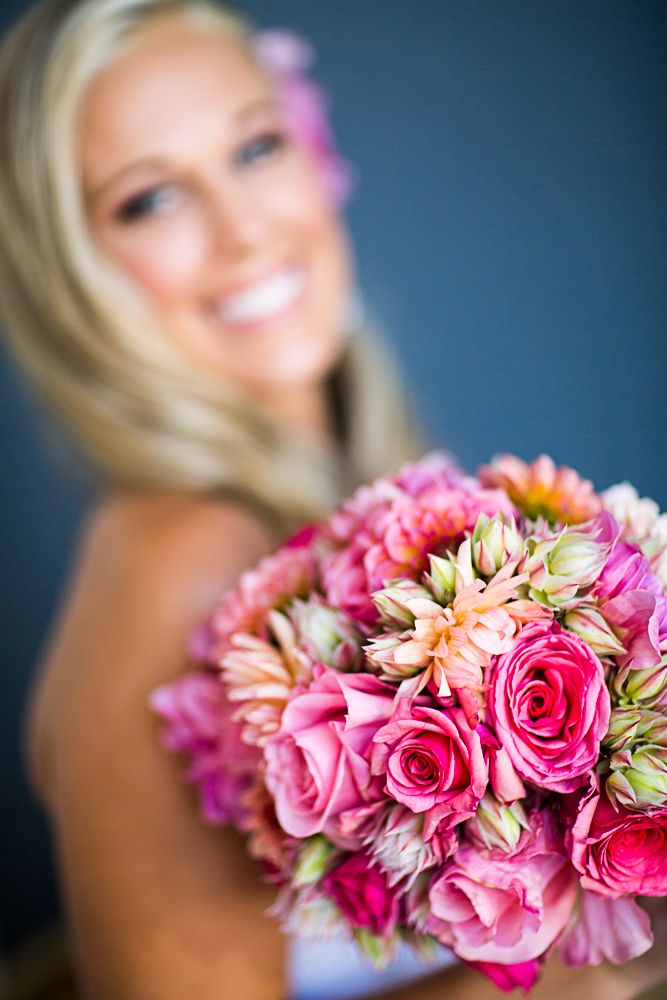 A row of colorful wedding bouquets featuring pink, orange, purple and yellow flowers with greenery against a soft light background.