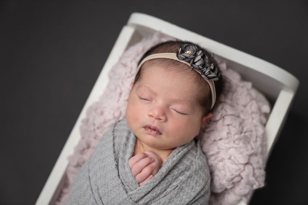 Sleeping newborn wrapped in gray swaddle wearing silver crown on textured backdrop.