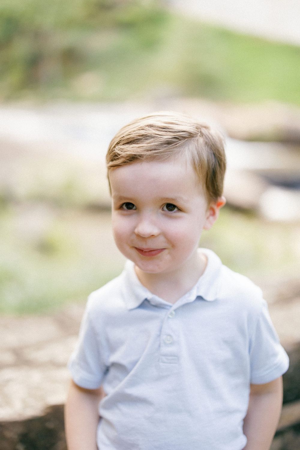 A child in a white polo shirt poses outdoors against a blurred natural background.