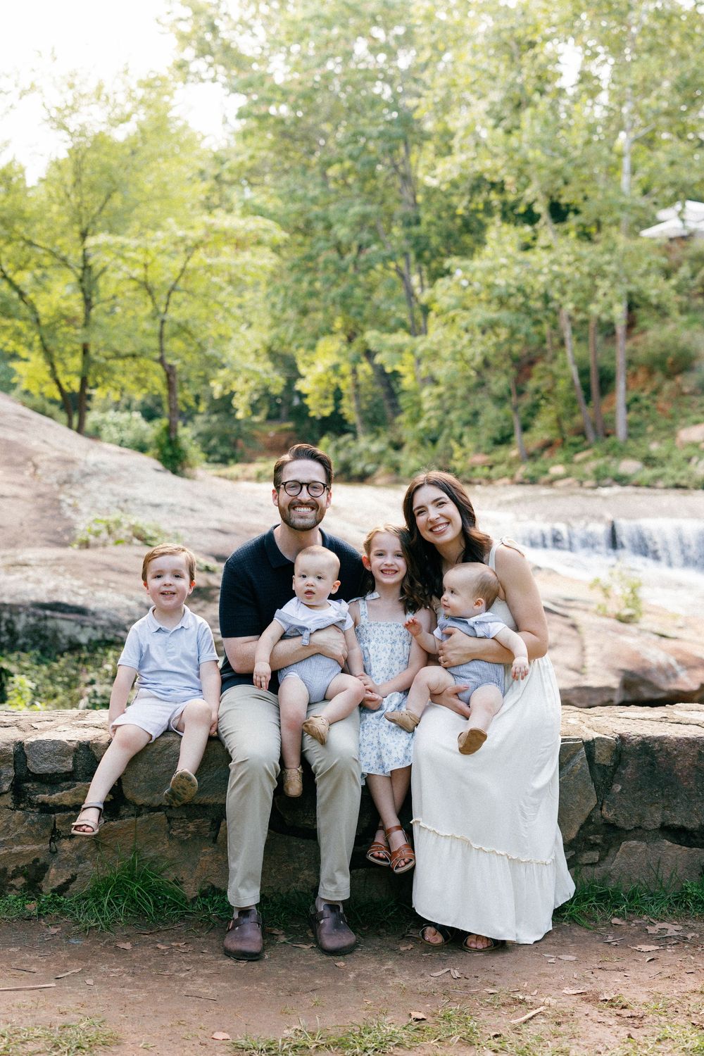 A casual outdoor portrait session with a family sitting together on stone steps in matching white and beige outfits.