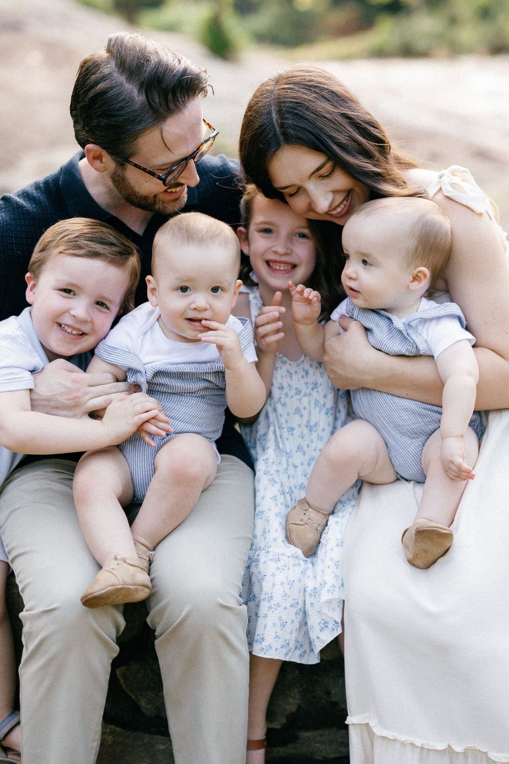 A joyful family with four children sits together and embraces on a sunny day outdoors.