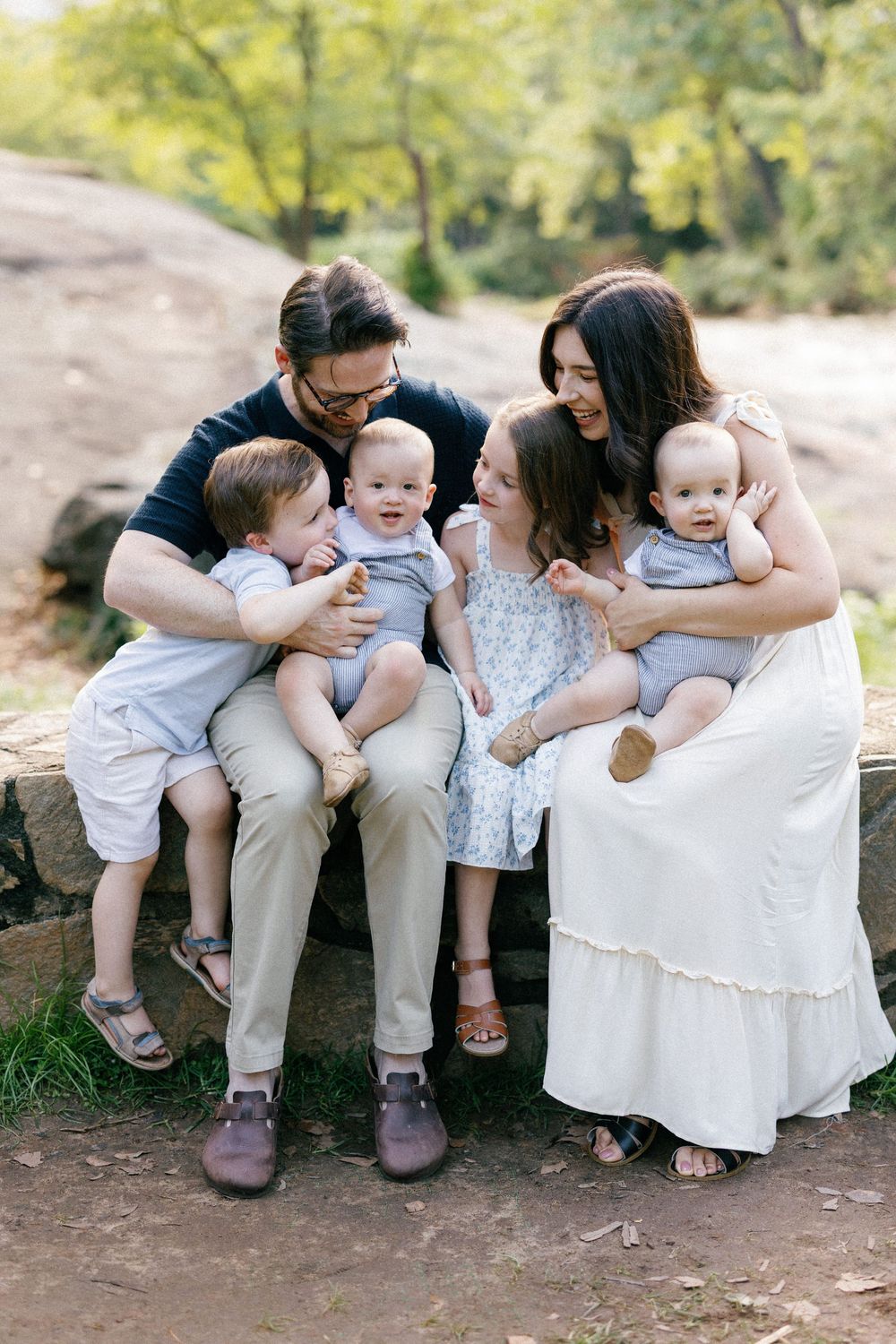 A family sits together on stone steps in coordinated outfits of white and blue during an outdoor photo session.