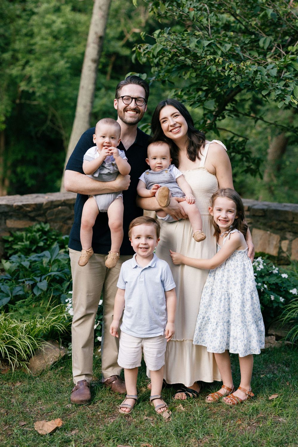 A family of six poses together outdoors in coordinated outfits against a lush green backdrop.
