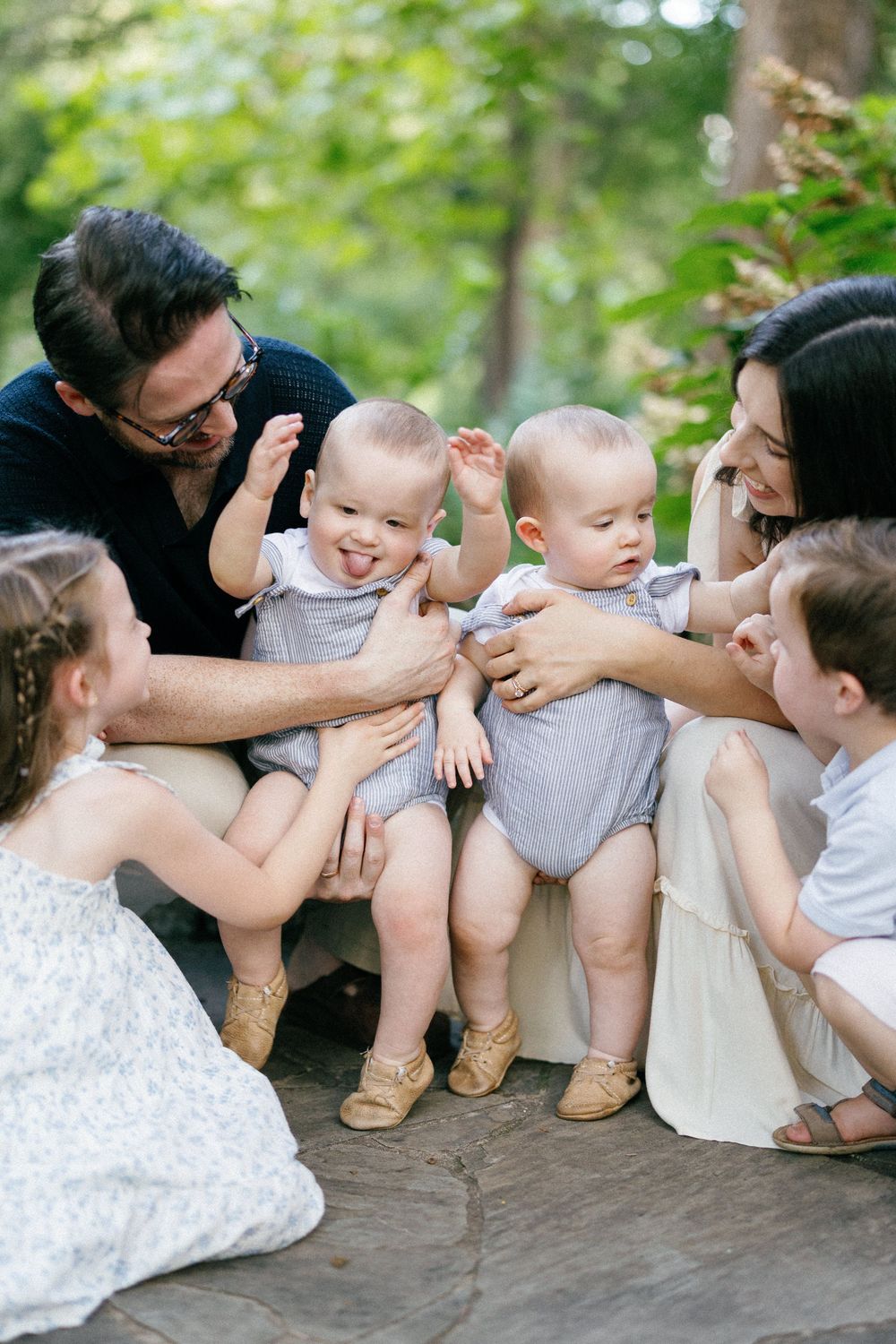 Candid family photoshoot showing playful interactions between loved ones on a nature path with lush greenery behind them.