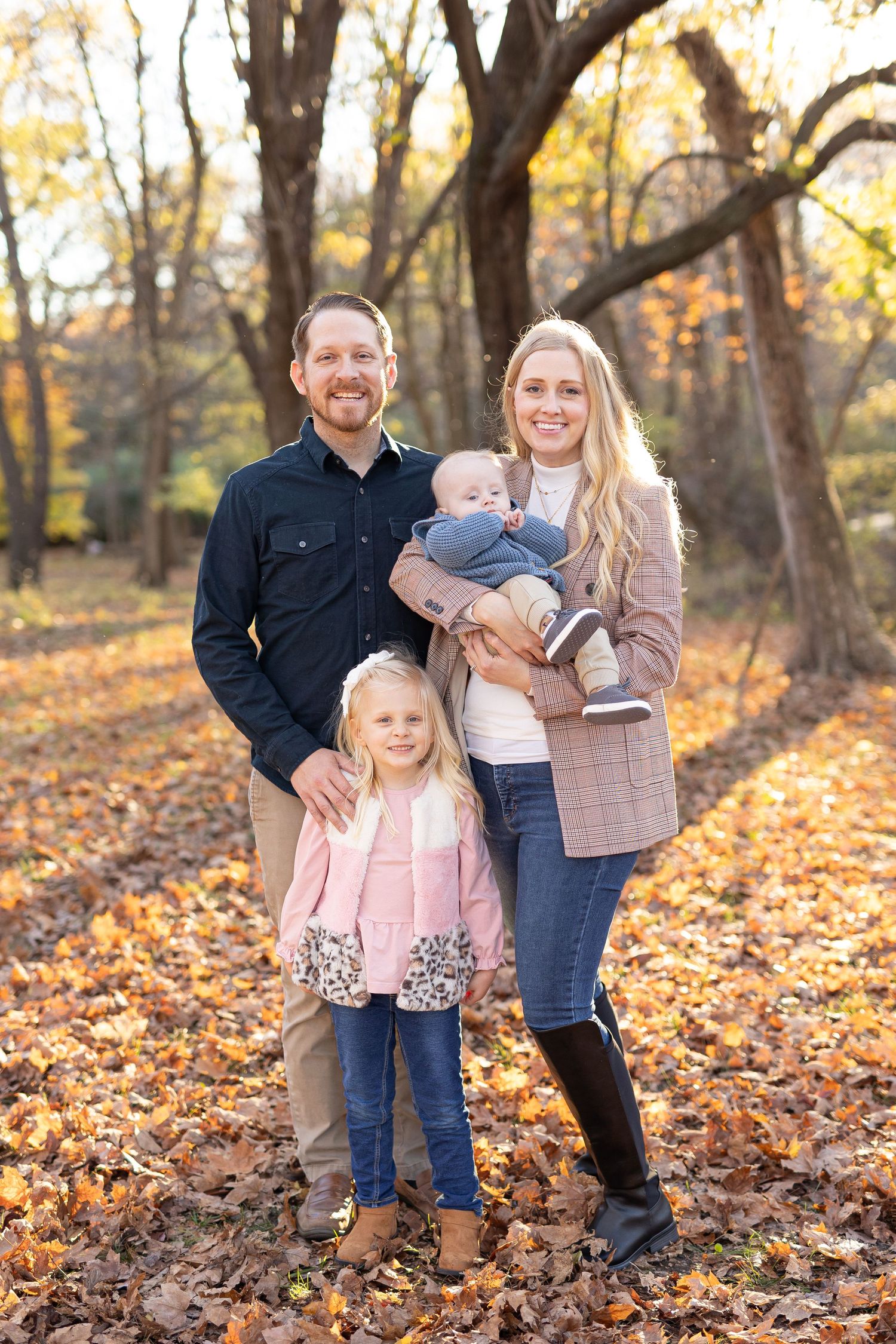 Family of four standing together against a cozy fall backdrop