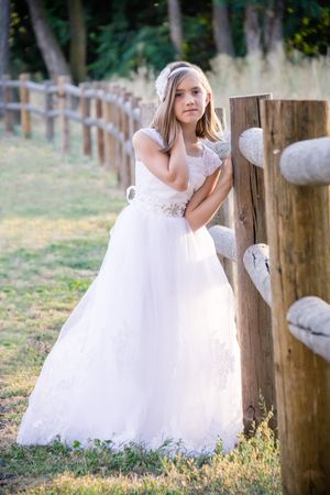 White dress flowing in breeze against rustic wooden fence posts at sunset.