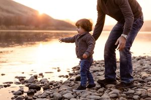 Family exploring rocky riverbank during golden hour sunset.