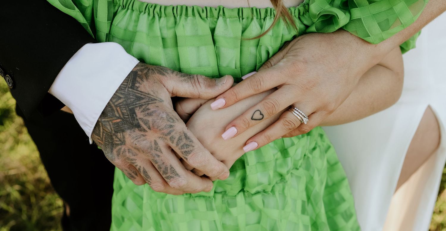 A pair of hands with floral tattoos gently touches a bright green fabric dress.
