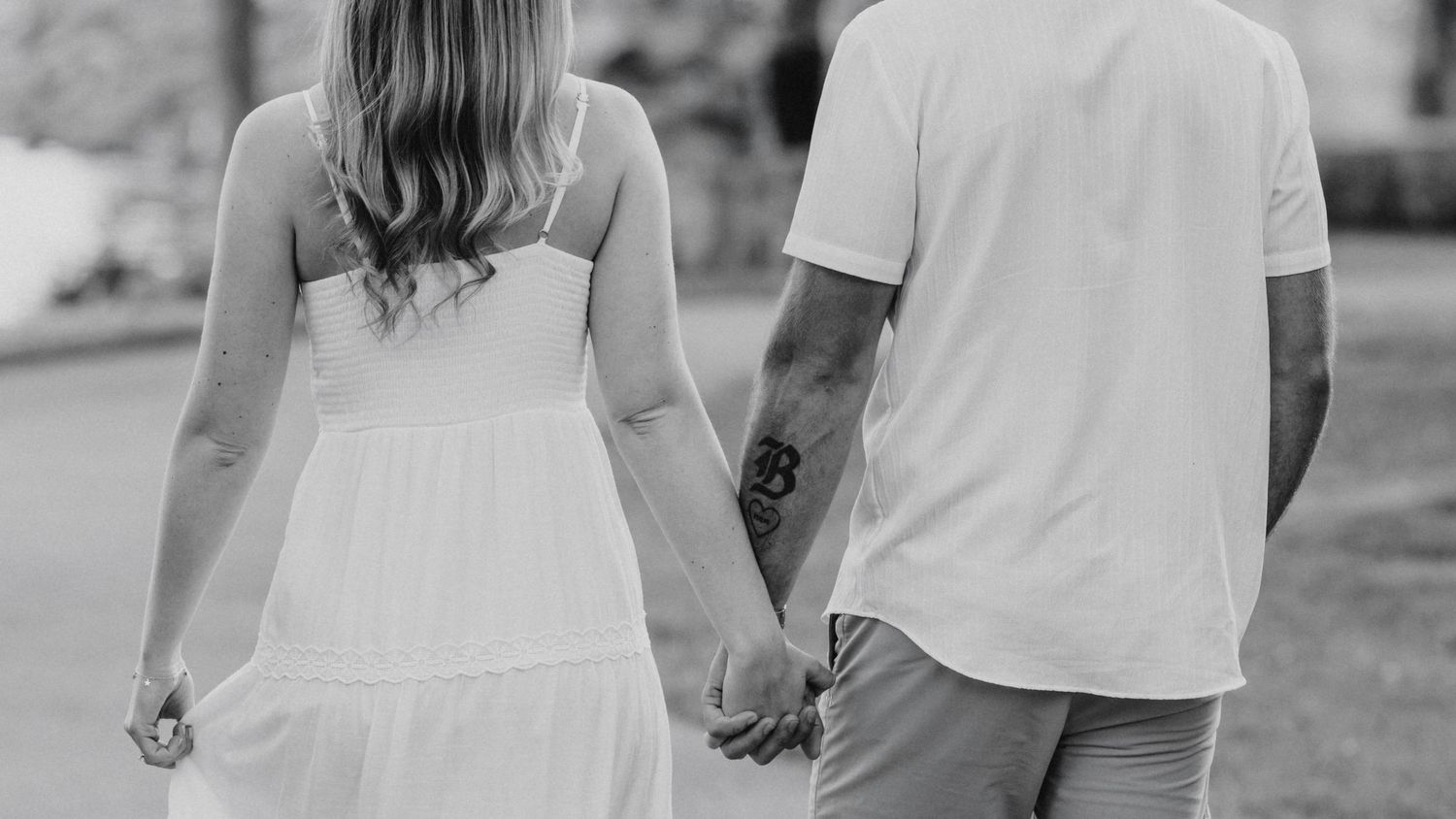 A couple holding hands while walking together outdoors in a black and white photograph.