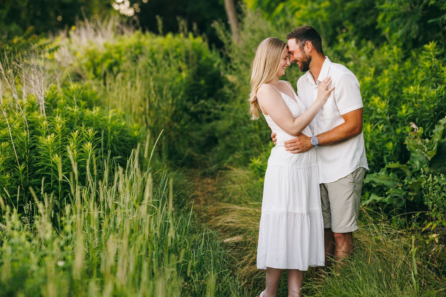 A couple embraces on a winding garden path surrounded by lush summer greenery and wildflowers.