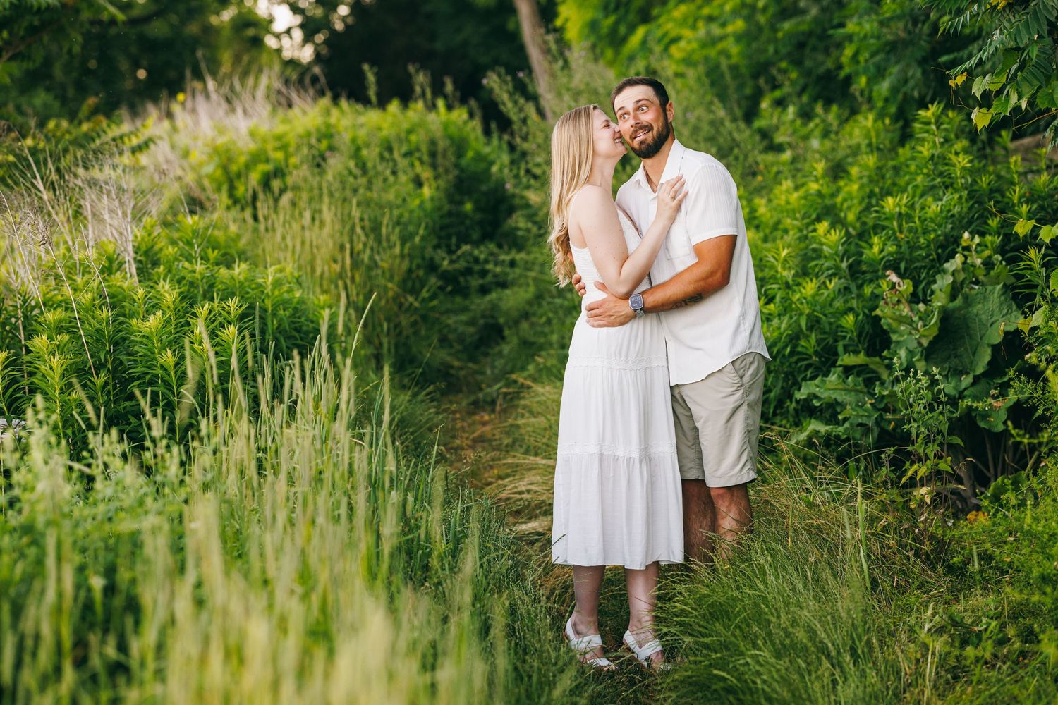 A romantic moment shared between a couple standing on a garden trail amidst tall green grasses.