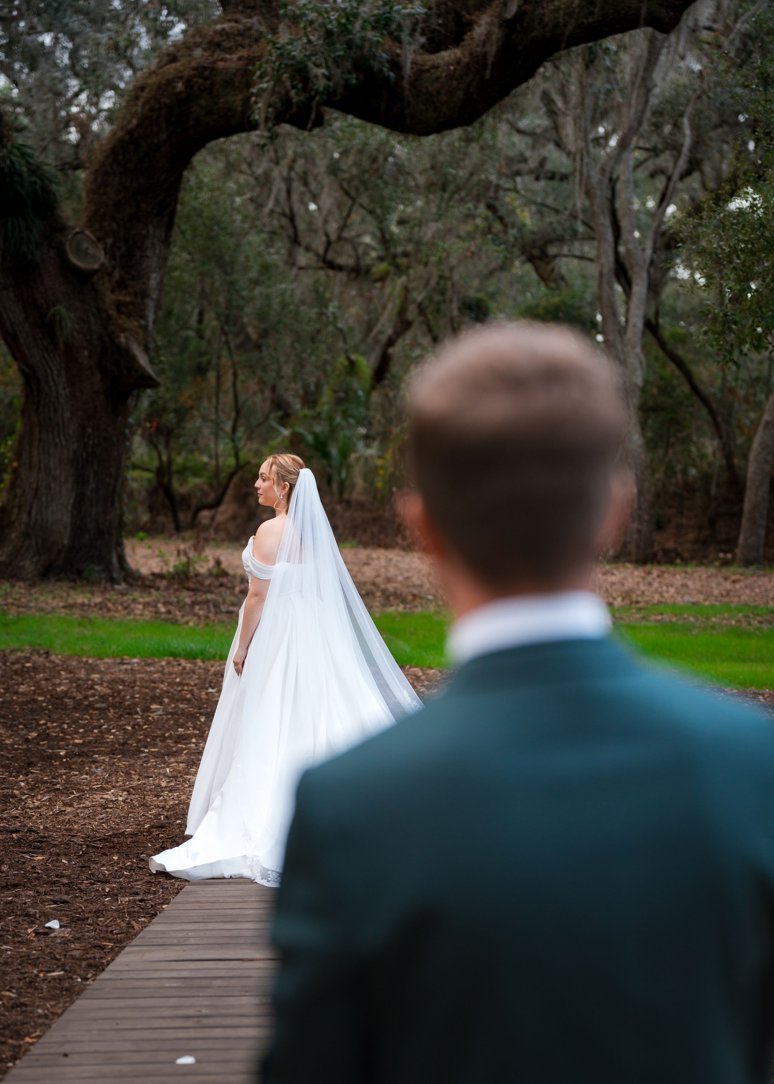 A couple shares a romantic moment on a wooden boardwalk surrounded by twisted oak trees and natural scenery.