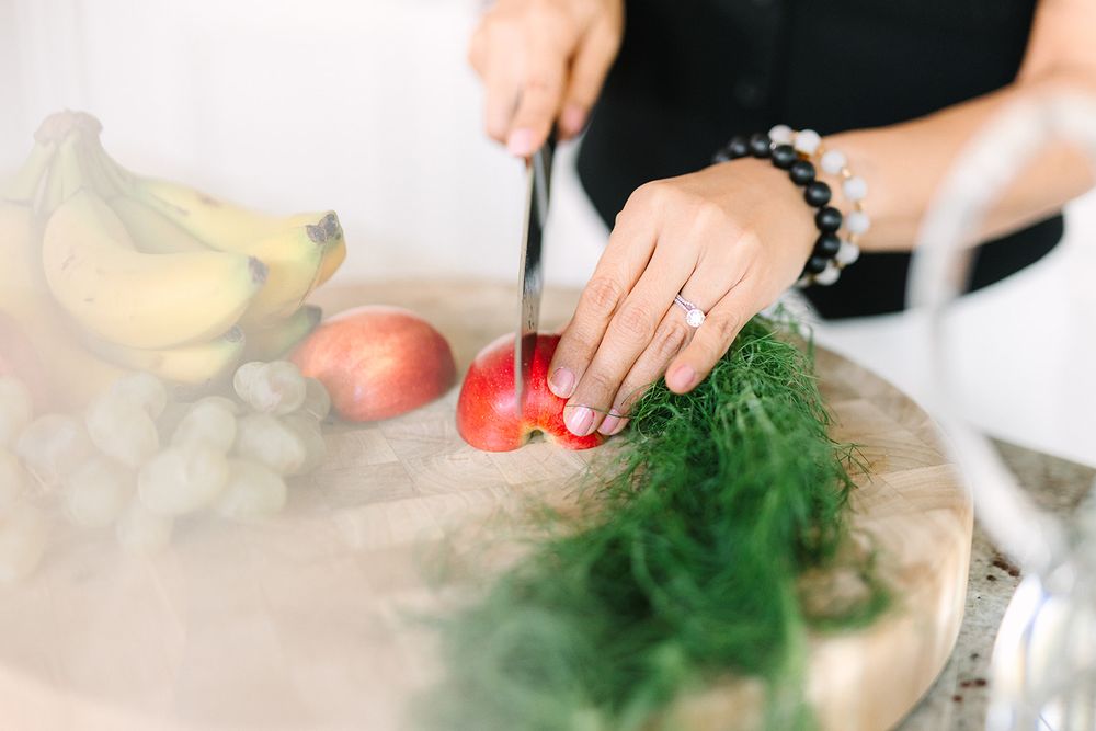 Close-up view of hands slicing fresh tomato on a cutting board with other produce and ingredients in the background.