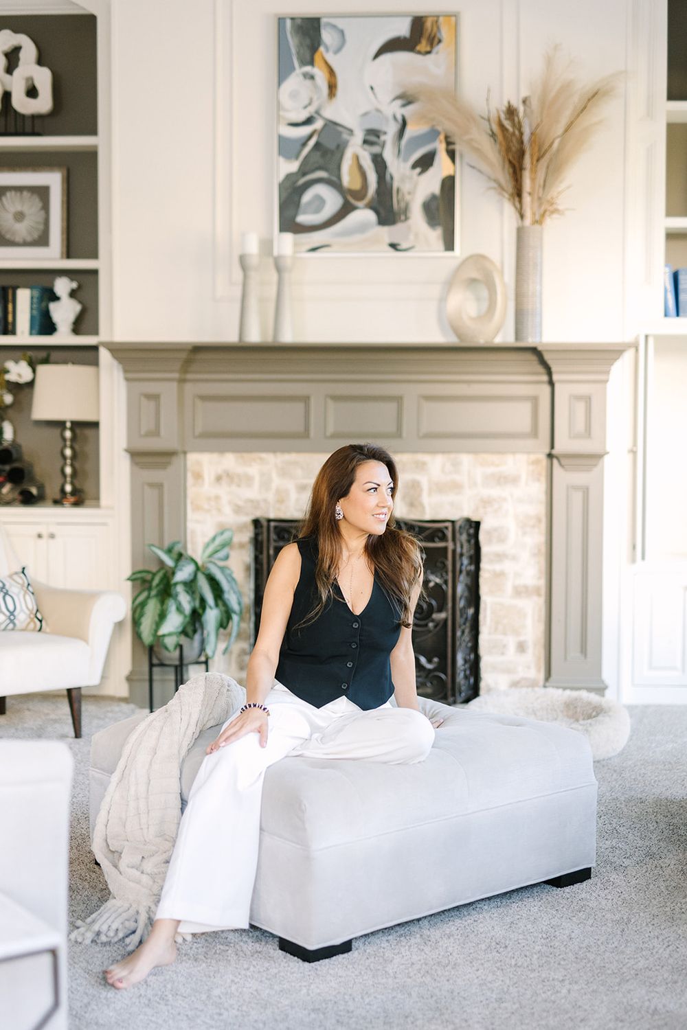 Elegant living room interior with abstract art, stone fireplace, and comfortable gray ottoman against white walls.