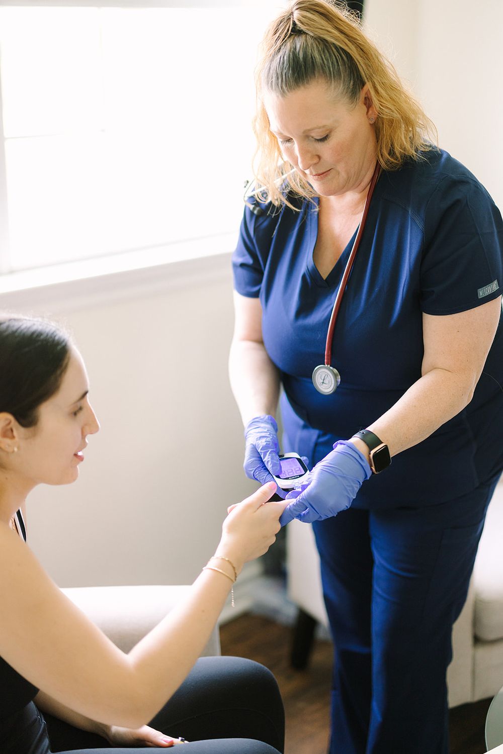 Healthcare provider in navy blue scrubs examines patient's arm during medical consultation in bright office.